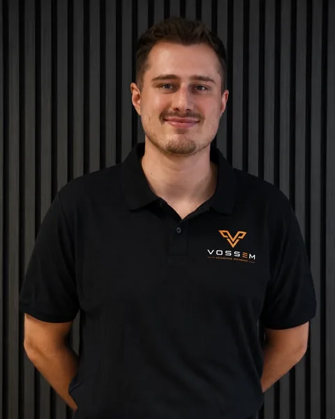 Mike Voss, Geschäftsführung und Head of Production bei Vossem, im Vossem-Poloshirt vor dunkler Lamellenwand