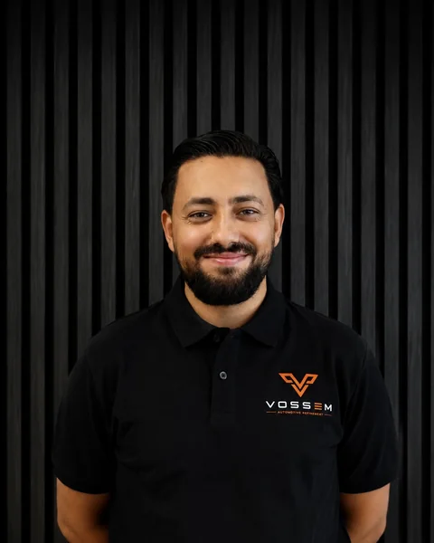 Mohammed Alkassem, Geschäftsführung und Administration bei Vossem, im Vossem-Poloshirt vor dunkler Lamellenwand