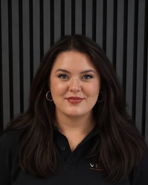 Tanja Köppen, Social Media und Kundenbetreuung bei Vossem, im Vossem-Poloshirt vor dunkler Lamellenwand